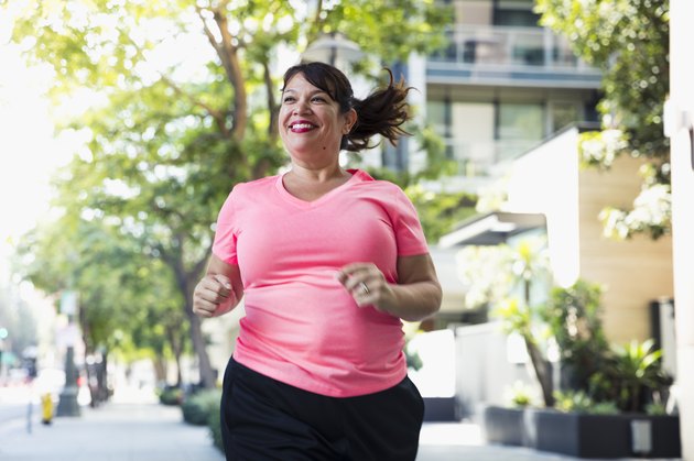 Cheerful woman jogging on footpath in city