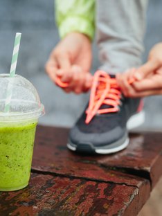 Sports nutrition smoothie next to person tying shoes before workout