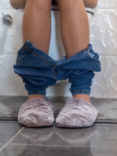 The view of a women in fuzzy slippers sitting on a toilet 