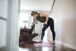 woman strength training with a kettlebell at home with her dog