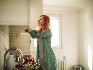红发女人在厨房橱柜里找东西。
