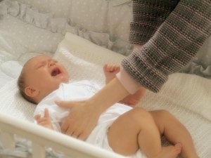 母亲伸手去抓婴儿床里哭泣的婴儿