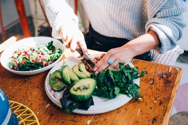 Woman chopping salad and avocados on a plate.