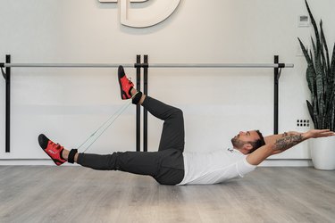 Man Doing Hollow Body Alternating Leg Squeeze With Resistance Band