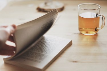 person reading book while drinking tea