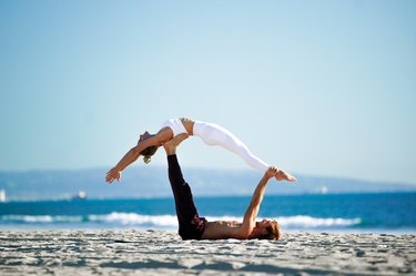 沙滩上的一对Acroyoga情侣，女士在做背部伸展。