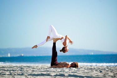 在海滩上，一名女子在她的瑜伽搭档的脚上做后弯。