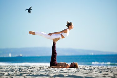 Woman performing back extension on partners feet on the beach.