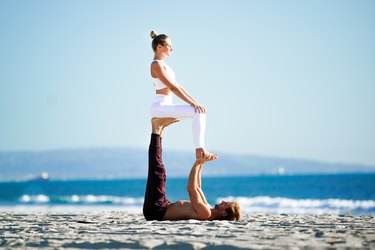 Woman sitting upright on partner's feet in an acroyoga pose on the beach.