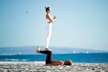 Woman standing on partner's shins on the beach.