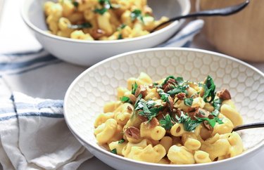 Two bowls of golden macaroni noodles topped with parsley and almonds.