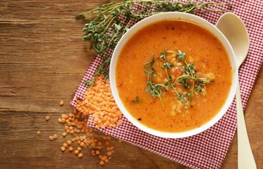 Red Lentil Soup with Lemon in a white bowl over red plaid tablecloth on wooden table.