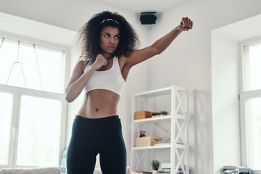 a person wearing black leggings and white sports bra doing a boxing workout at home without equipment