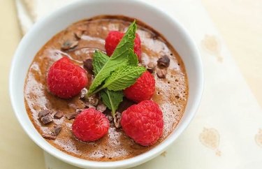 Vegan Chocolate Mousse in a white bowl with raspberries and green leafy garnish