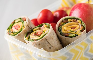 Greens, fruit and chickpea wraps in plastic container with apple