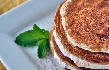 Tiramisu Protein Pancakes With Banana-Cream Frosting on a white plate with a leafy garnish