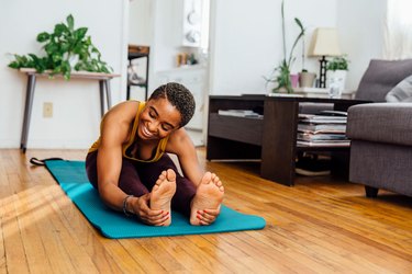 smiling woman does a seated forward fold to touch toes