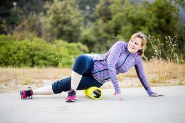 middle-aged woman doing foam rolling on her hip outdoors