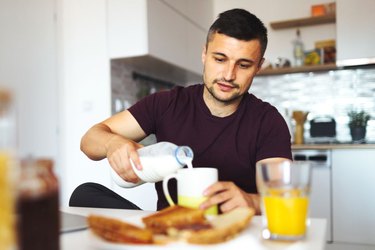 Man pouring glass of milk at breakfast.