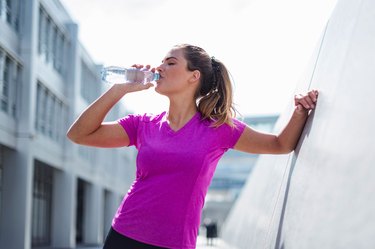 Woman taking a break during workout to hydrate with water as a way to reduce body fat percentage
