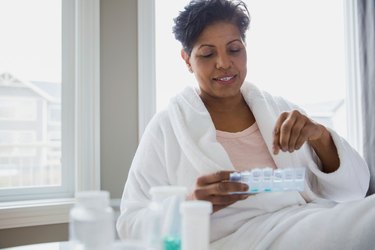Middle-aged woman in white robe taking morning pills from pill case