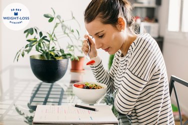 Woman eating breakfast and reading food journal