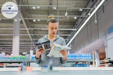 A person with a blonde bun wearing a gray hoodie reading nutrition labels on frozen food items in a supermarket