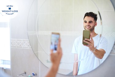 A man taking a photo of himself in the mirror to track weight loss without a scale