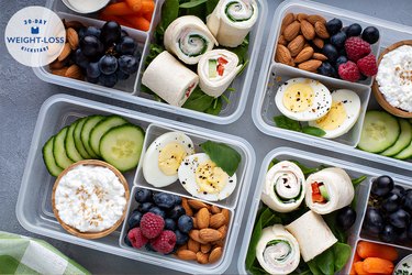 meal prepped lunches in containers with hard boiled eggs cucumbers and fresh fruit and nuts
