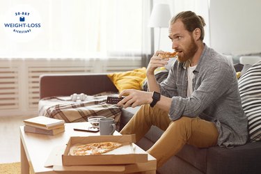 man sitting on couch eating pizza and holding TV remote