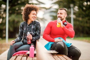 Couple on bench drinking energy drinks.