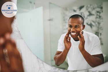 A smiling man looking at his reflection in the bathroom mirror after losing weight