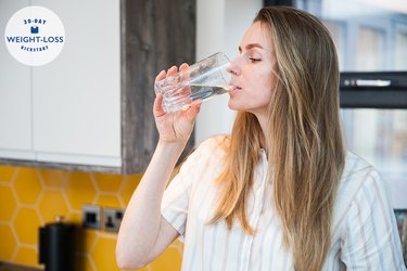 A woman drinking a glass of water in her kitchen at home