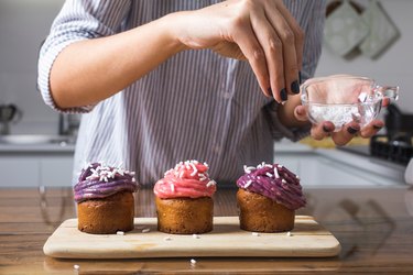 Woman putting sprinkles on sugary cupcakes