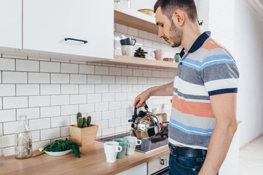 Young man prepare breakfast with tea pour water from kettle in kitchen.