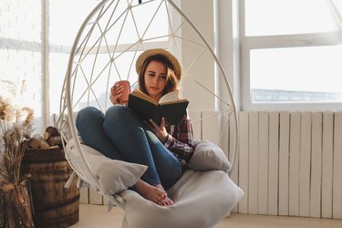 woman sitting on chair reading book and sipping dandelion tea