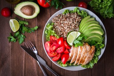 Healthy salad bowl with quinoa, tomatoes, chicken, avocado, lime and mixed greens (lettuce, parsley) on wooden background top view. Food and health