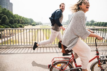 Woman riding bike, man running after her laughing