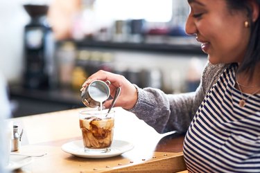 Woman in cafe pouring coffee creamer in iced coffee