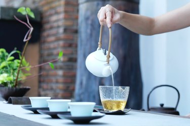Person's hand pouring green tea into glass from white teapot for health benefits of tea