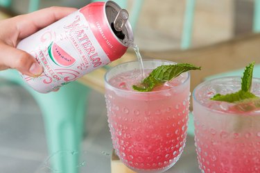 hand pouring watermelon sparkling water into glass with pink drink