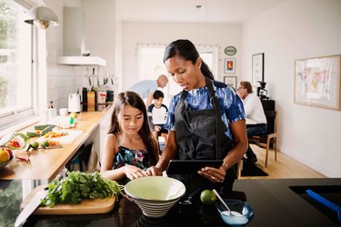 Woman and daughter in kitchen cooking from recipe with cooking tips and cooking hacks