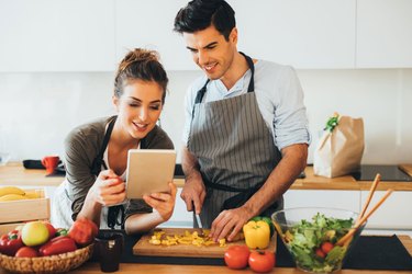 Woman and man in kitchen using cooking tips on ipad