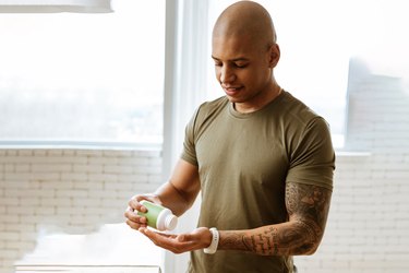 Athletic man taking supplements in kitchen