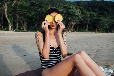 woman sitting on a beach playing with pineapple slices