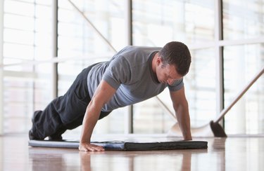 Man holding a plank over a mat in the gym.
