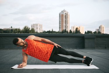 Man doing a side plank on urban rooftop outside.