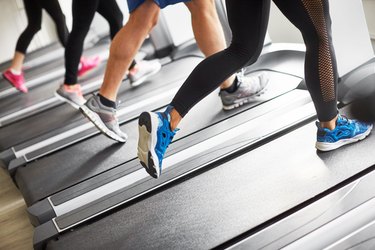 Group of people jogging on treadmills at the gym, legs and sneakers shown