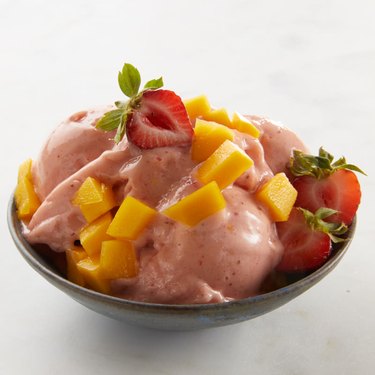 Pink ice cream topped with mango chunks and halved strawberries
