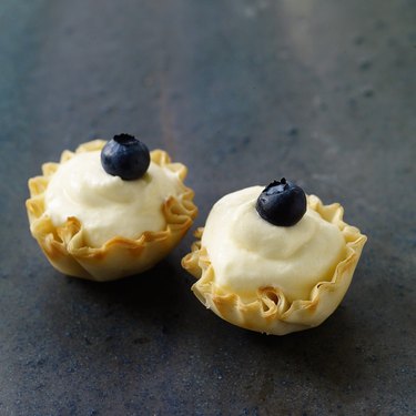 Two little berry lemon tartlets, each topped with a blueberry